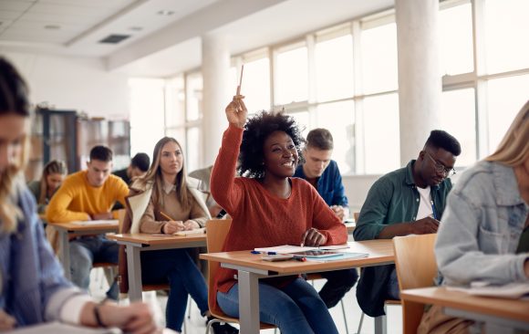 Happy black student raising arm to answer question while attending class with her university colleagues. Igniting a Passion for Lifelong Learning Through Afrocentric Education